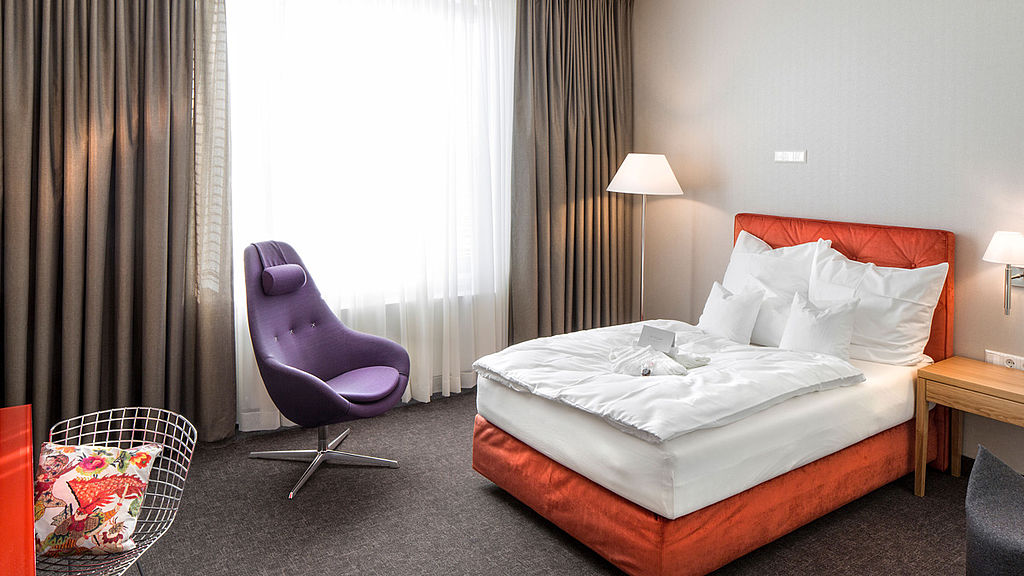 Hotelzimmer mit orangefarbenen Bett und lila Sessel